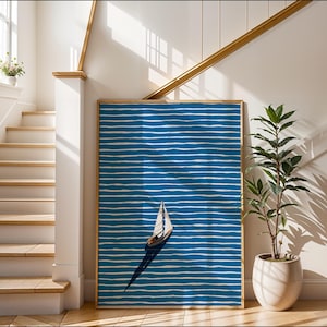Puede incluir: Una impresi&oacute;n art&iacute;stica enmarcada que presenta un velero sobre un fondo a rayas azules y blancas. La obra de arte se exhibe en un pasillo luminoso con una escalera y una planta en maceta. El marco es de color madera clara.