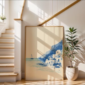 May include: A framed art print depicts a coastal scene with a sailboat, buildings, and a mountain in shades of blue and beige. The artwork is displayed against a white wall next to a staircase and a potted plant.