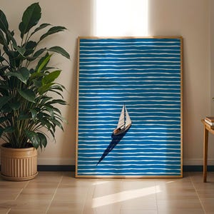 Puede incluir: Una impresi&oacute;n art&iacute;stica enmarcada que presenta un velero sobre un fondo a rayas azules y blancas. La obra de arte tiene un marco de madera y se exhibe en una habitaci&oacute;n bien iluminada con una gran planta en maceta y una mesita auxiliar.