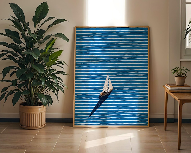 Puede incluir: Una impresi&oacute;n art&iacute;stica enmarcada que presenta un velero sobre un fondo a rayas azules y blancas. La obra de arte tiene un marco de madera y se exhibe en una habitaci&oacute;n bien iluminada con una gran planta en maceta y una mesita auxiliar.