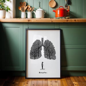 May include: Black framed art print featuring a stylized illustration of lungs formed by trees. A small figure stands below the lungs. The word "Breathe" is printed at the bottom of the print.