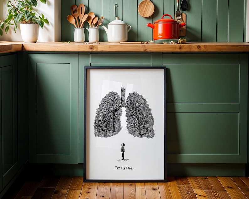May include: Black framed art print featuring a stylized illustration of lungs formed by trees. A small figure stands below the lungs. The word "Breathe" is printed at the bottom of the print.