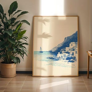 May include: A framed art print depicting a coastal scene with a sailboat on the water and buildings on a hillside. The artwork is in shades of blue and beige, with a wooden frame. A large potted plant is to the left.