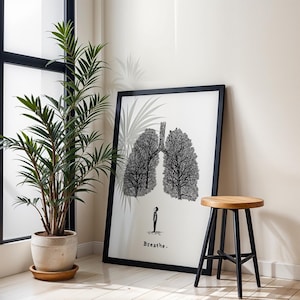 May include: A framed art print featuring a black and white illustration of lungs made of trees, with the word "Breathe" below. A wooden stool with black legs and a potted plant are in the foreground.