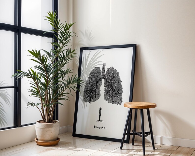 May include: A framed art print featuring a black and white illustration of lungs made of trees, with the word "Breathe" below. A wooden stool with black legs and a potted plant are in the foreground.