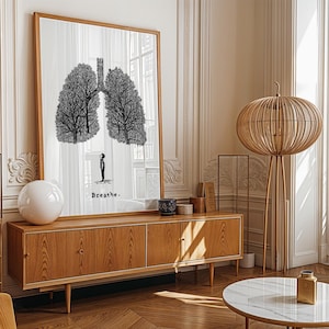 May include: A large framed art print featuring a black and white illustration of lungs shaped like trees, with a small figure below. The word "Breathe" is written below the figure. The artwork is displayed above a wooden cabinet.