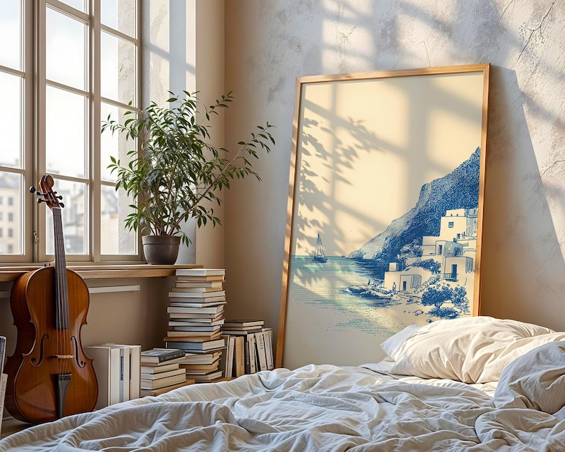 May include: A framed print of a coastal scene with blue and white buildings, a mountain, and a sailboat. The artwork is displayed in a room with a cello, a potted plant, and a stack of books. The room has a large window and a bed with white bedding.