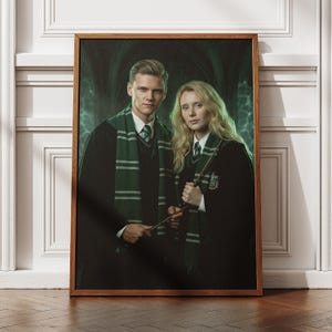 May include: A framed portrait featuring two individuals in dark robes and green and silver striped scarves. They hold wands and stand against a green, blurred background. The frame is a warm brown color.