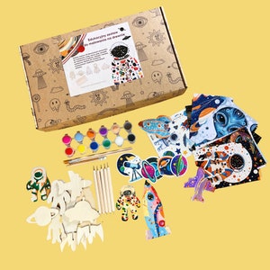 May include: A space-themed craft kit with wooden shapes, paint, brushes, and stickers. The box features the text "Edukacyjny zestaw do malowania na drewnie" which translates to "Educational set for painting on wood".