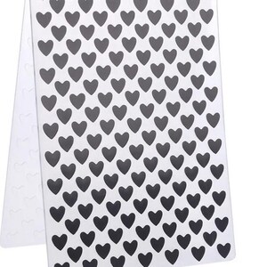 Puede incluir: Una carpeta de relieve rectangular de plástico transparente con un patrón repetitivo de formas de corazón de color gris oscuro dispuestas en filas uniformes, diseñada para crear impresiones texturizadas en papel o cartulina.
