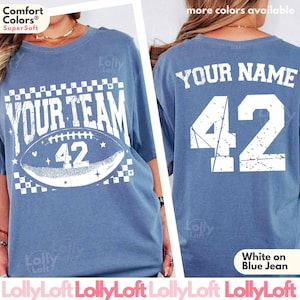 May include: A blue jean-colored t-shirt with white text and graphics. The front of the shirt says "YOUR TEAM" above a football graphic with the number "42". The back of the shirt has "YOUR NAME" above the number "42".