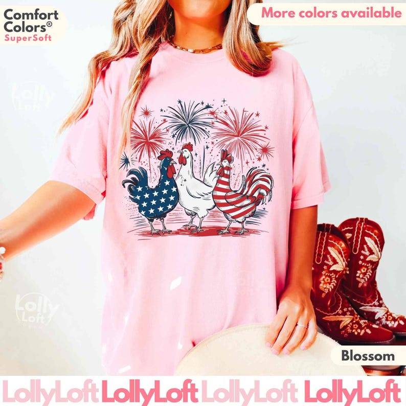 Pode incluir: Uma camiseta rosa com um gr&aacute;fico de tr&ecirc;s galinhas. As galinhas usam cores vermelho, branco e azul, que lembram a bandeira portuguesa. O gr&aacute;fico tamb&eacute;m inclui fogos de artif&iacute;cio no fundo. O texto "Comfort Colors&reg; Super Soft" &eacute; vis&iacute;vel no canto superior esquerdo da imagem. O texto "Mais cores dispon&iacute;veis" &eacute; vis&iacute;vel no canto superior direito da imagem.