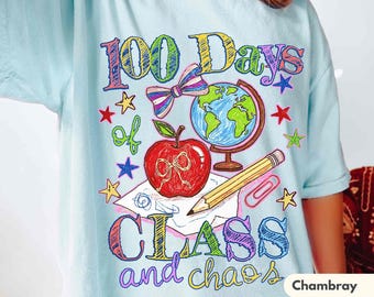May include: A light blue t-shirt featuring a colourful graphic with the text 100 Days of CLASS and chaos. The design includes a red apple, a globe, a pencil, a paperclip, a bow, and various stars in a scribbled, crayon-like style.