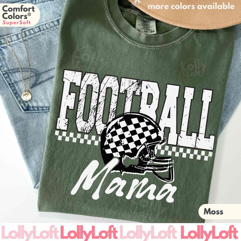 May include: Moss green t-shirt with the words "FOOTBALL Mama" in white, featuring a checkered football helmet graphic. The shirt is made of a soft material and is displayed with blue jeans and a necklace.
