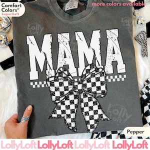 Op de afbeelding: Een grijs Comfort Colors Super Soft t-shirt met het woord "MAMA" in grote witte, versleten letters. Een zwart-wit geblokte strik staat eronder. Het shirt is gelabeld met "Pepper" en "meer kleuren beschikbaar".