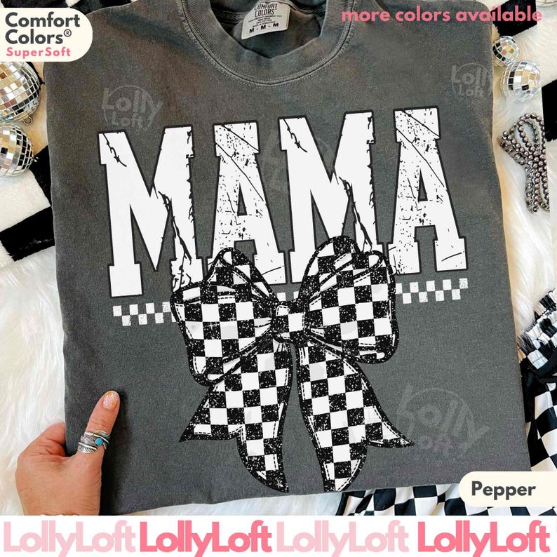 Op de afbeelding: Een grijs Comfort Colors Super Soft t-shirt met het woord "MAMA" in grote witte, versleten letters. Een zwart-wit geblokte strik staat eronder. Het shirt is gelabeld met "Pepper" en "meer kleuren beschikbaar".
