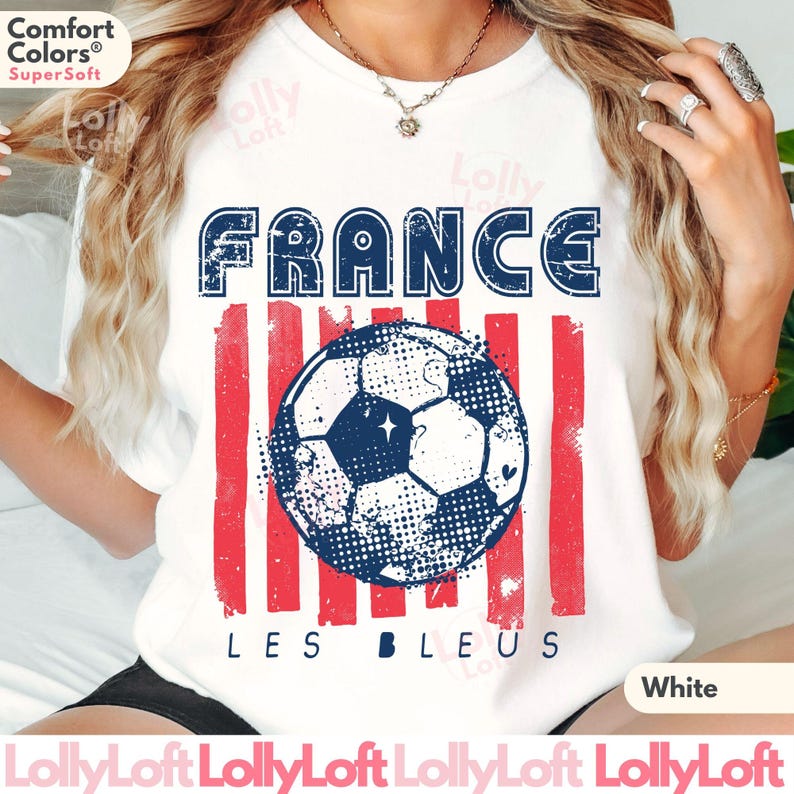May include: White t-shirt with a distressed design featuring the word "FRANCE" in blue, red stripes, and a soccer ball graphic. The text "LES BLEUS" is below the soccer ball. The shirt is made of a soft material.