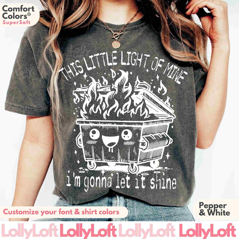 Pu&ograve; includere: Una maglietta grigia con una grafica bianca di un cassonetto dei rifiuti di cartone in fiamme con il testo "This little light of mine I'm gonna let it shine".