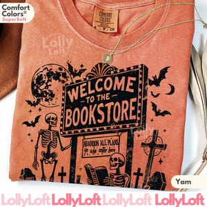 May include: A yam-colored t-shirt with a graphic that reads "WELCOME TO THE BOOKSTORE." The design includes bats, skeletons, a full moon, and crosses. The shirt has a crew neck and a Comfort Colors tag.