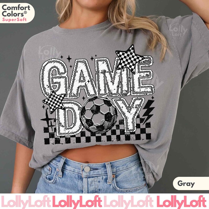 May include: Gray t-shirt with the words "GAME DAY" in a white, outlined font, featuring a soccer ball and checkered star accents. The shirt is made of a soft material and is a comfortable fit.