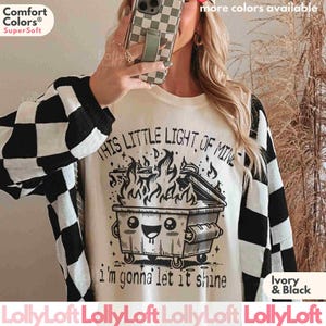Pu&ograve; includere: Maglietta bianca con una grafica in bianco e nero di un cassonetto in fiamme con il testo "This little light of mine - I'm gonna let it shine".