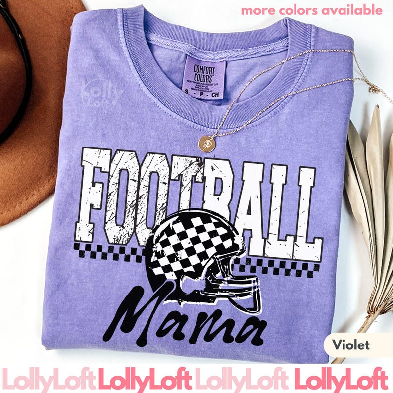 May include: A violet Comfort Colors t-shirt with the words "FOOTBALL Mama" in white and black. The design includes a football helmet with a checkered pattern. A gold necklace is draped on the shirt. The text "more colors available" is at the top.