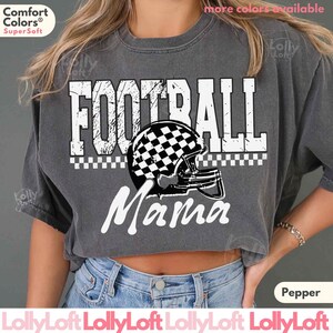 May include: A gray Comfort Colors t-shirt with the words "FOOTBALL Mama" in white. The design includes a football helmet with a checkered pattern. The shirt is a Pepper color.