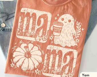 May include: A terracotta-coloured t-shirt featuring a distressed white graphic print. The design includes the word MAMA, a ghost holding a cup labelled PUMPKIN LATTE, and a pumpkin illustration. The shirt has a Comfort Colors tag at the neckline.