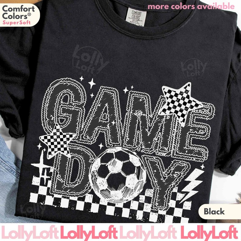 May include: Black t-shirt with a white graphic that says "GAME DAY" with a soccer ball in the center. The design includes stars and a checkered pattern. The shirt is made of a soft material.