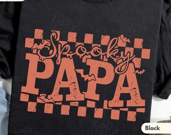 May include: A black short-sleeved t-shirt featuring a distressed orange graphic print. The design includes a checkered background, small bat silhouettes, and the text "Spooky PAPA" in a stylised font. The shirt has a crew neckline.
