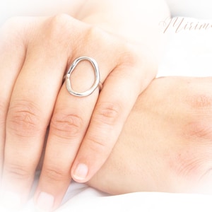 Peut inclure: Une bague en argent avec une forme ovale simple. La bague est portée au doigt.