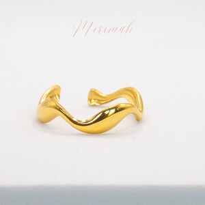 May include: A gold-coloured, wavy, open ring. The ring is made of metal and has a smooth, polished finish.