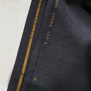 Könnte beinhalten: Nahaufnahme von dunkelgrauem Stoff mit einem gold- und grün gewebten Etikett mit der Aufschrift "120'S SUPER WOOL".