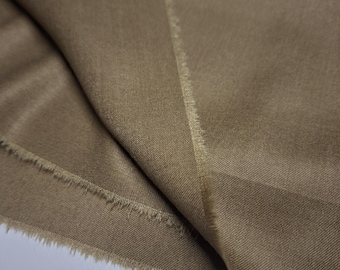 May include: Close-up of a folded piece of tan fabric. The fabric has a smooth texture and a slight sheen. The edges of the fabric are frayed, revealing the weave. The color is a warm, neutral tone, suitable for various sewing projects.