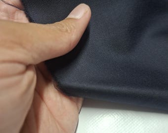 May include: Close-up of a piece of navy blue fabric. The fabric has a smooth texture and a raw edge. The fabric is being held by a hand.