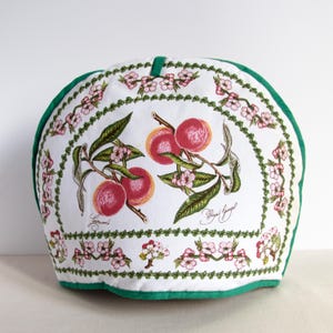 Puede incluir: Cubierta de tostador de algodón blanco con borde verde. La cubierta presenta un diseño de melocotón con flores rosas y hojas verdes. El texto "Signora" y "Flora & Fauna" está impreso en la cubierta.