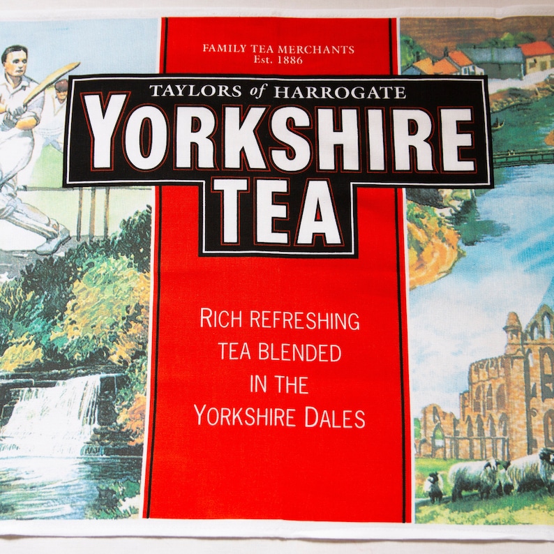 Puede incluir: Un pa&ntilde;o de cocina Yorkshire Tea rojo y blanco. El pa&ntilde;o presenta el nombre de la marca en letras blancas grandes sobre un fondo negro. Tambi&eacute;n hay ilustraciones de los Yorkshire Dales y jugadores de cr&iacute;quet.
