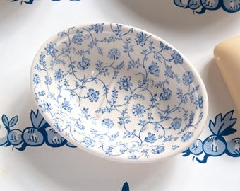 May include: Oval-shaped white ceramic soap dish with a blue floral pattern. The dish features a delicate design of blue flowers and vines, creating a vintage aesthetic. The soap dish is likely part of a bathroom decor set.