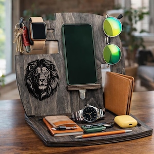May include: Wooden desk organiser with a lion head carving. It holds a smartphone, watch, wallet, keys, sunglasses, and other accessories. The organiser is made of dark wood and has a modern design.