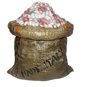 May include: A ceramic container shaped like a burlap sack, filled with white and pink pebble-like objects. The container is tan with orange accents and the words "MADE IN ITALY" are visible on the front.