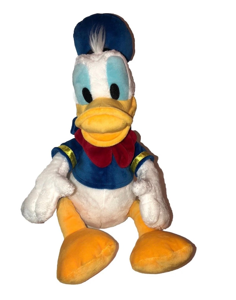 May include: A plush Donald Duck toy. The toy features a blue sailor hat, a blue sailor shirt with gold trim, a red bow tie, and yellow feet and beak. The toy has white feathers and blue eyes.