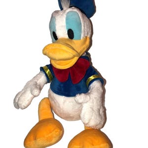 May include: A plush Donald Duck toy. The toy features a white body, a yellow beak and feet, and blue eyes. He wears a blue sailor shirt with gold trim and a red bow tie. A blue sailor hat sits atop his head.