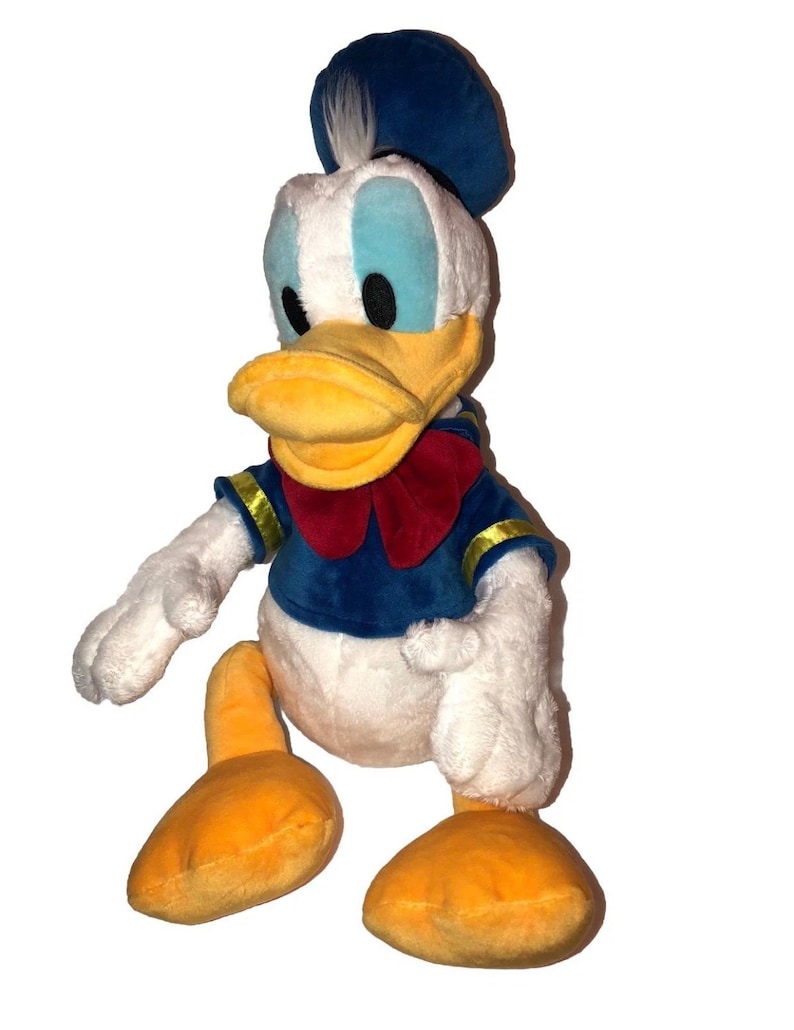 May include: A plush Donald Duck toy. The toy features a white body, a yellow beak and feet, and blue eyes. He wears a blue sailor shirt with gold trim and a red bow tie. A blue sailor hat sits atop his head.