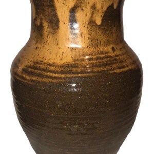 May include: A handcrafted ceramic vase with a two-tone glaze. The upper portion is a warm, light brown, transitioning to a darker, earthy brown at the base. The vase has a wide body and a slightly flared rim, showcasing a rustic aesthetic.