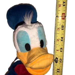May include: A plush Donald Duck toy, featuring a blue sailor hat, white face, and yellow beak. The toy is approximately 16 inches tall, with a red and blue outfit. A measuring tape is next to the toy.