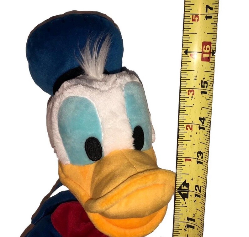 May include: A plush Donald Duck toy, featuring a blue sailor hat, white face, and yellow beak. The toy is approximately 16 inches tall, with a red and blue outfit. A measuring tape is next to the toy.