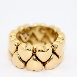 May include: A gold heart-shaped ring with a band made of interlocking hearts