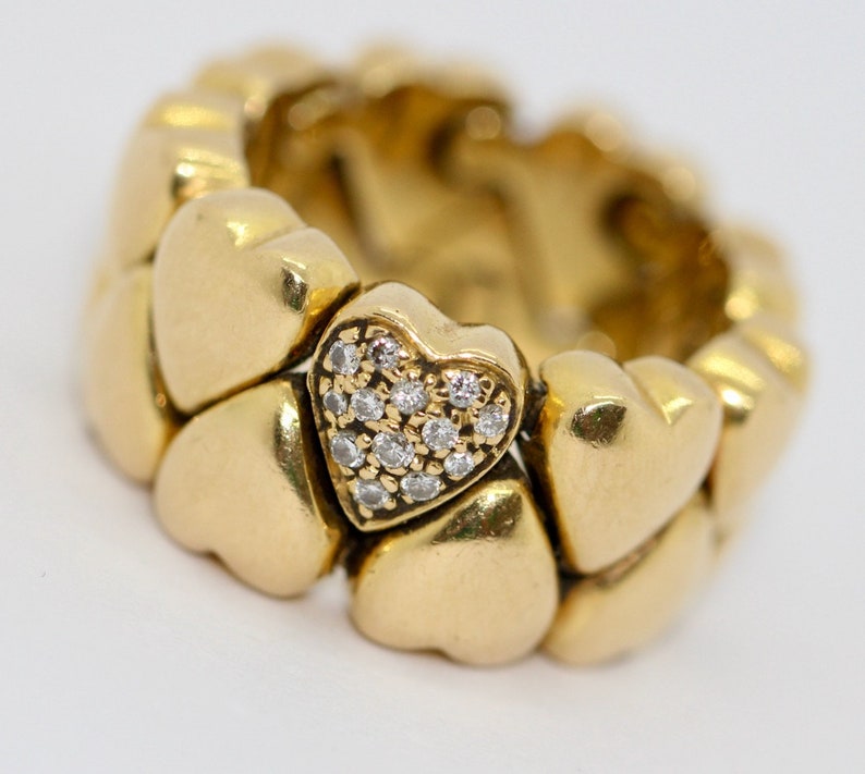 May include: A gold heart-shaped ring with a pave diamond heart in the center. The ring is made up of multiple connected heart shapes.