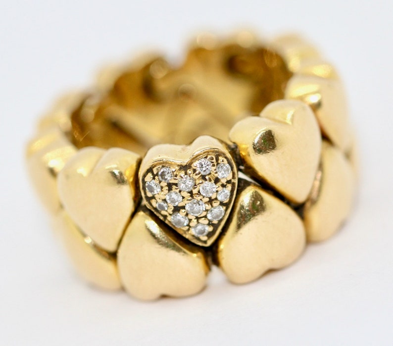 May include: A gold ring with a heart-shaped design. The ring is made up of multiple heart-shaped pieces, with a single heart in the center that is set with small diamonds.