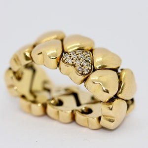 May include: A gold ring with a heart-shaped design. The ring is made of multiple heart-shaped pieces that are linked together. The ring has a small heart-shaped piece in the center that is set with diamonds.